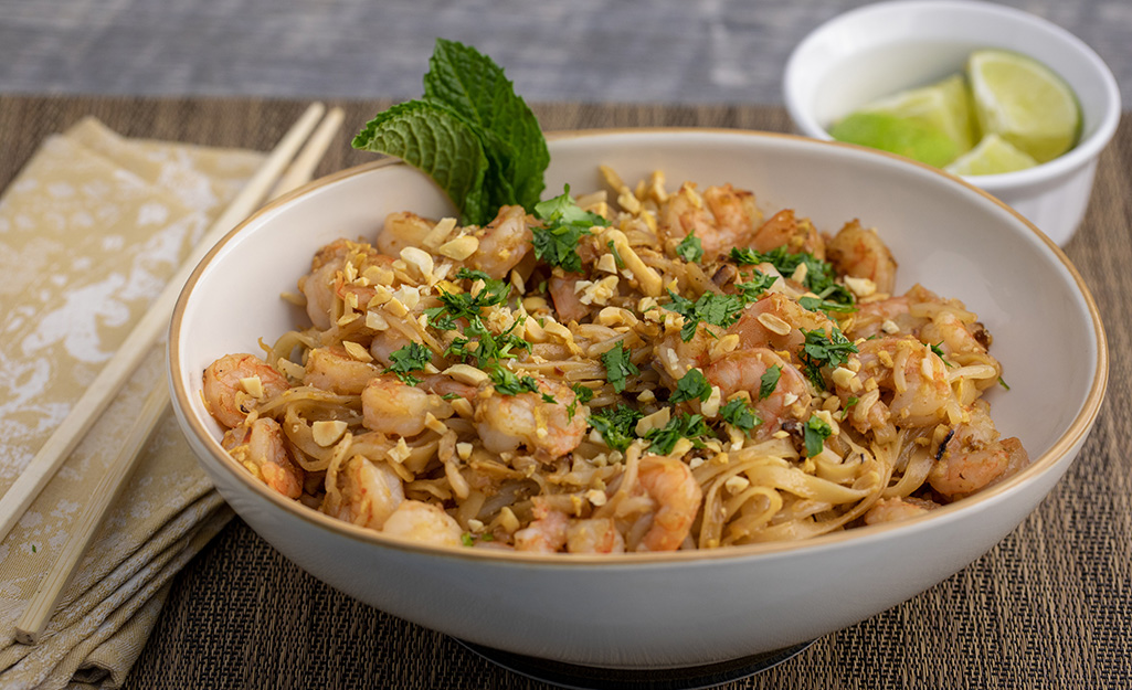 Shrimp pad Thai with cilantro in a white bowl with limes