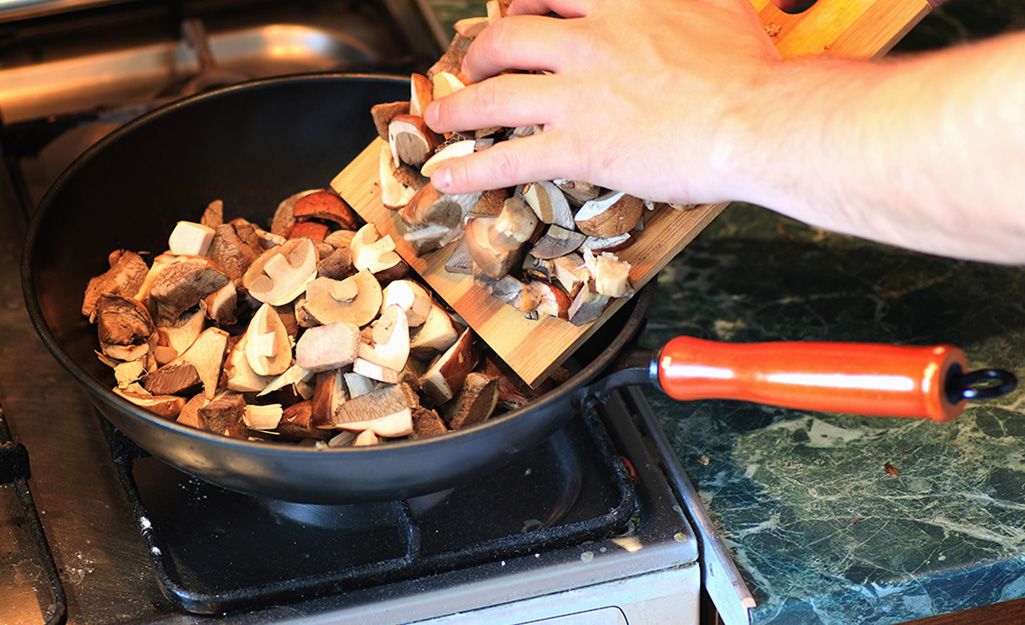 Person putting mushrooms into a skillet.