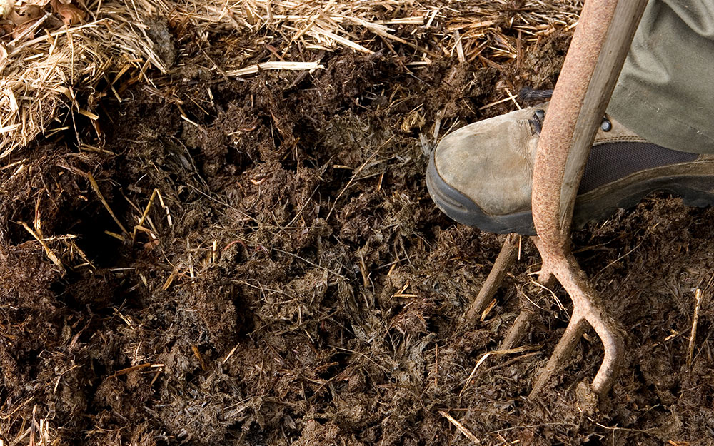 A person digging into soil with a garden fork.