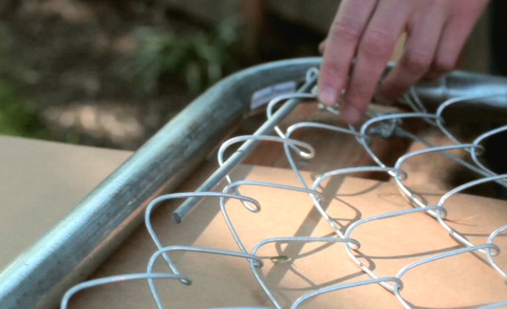 Someone adding a tension bar to a chain-link gate. Someone adding a tension bar to a chain-link gate.