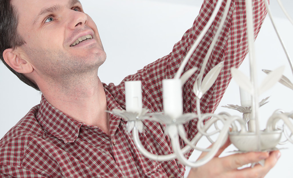 Man holding a chandelier as he hangs it.