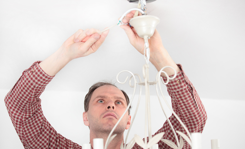 A person connects wiring from a chandelier to the ceiling.