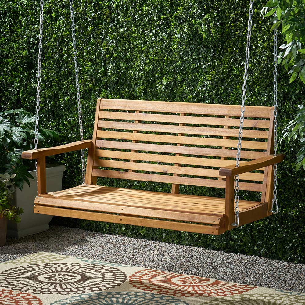 A wooden porch swing hangs from chains in front of a wall of greenery.