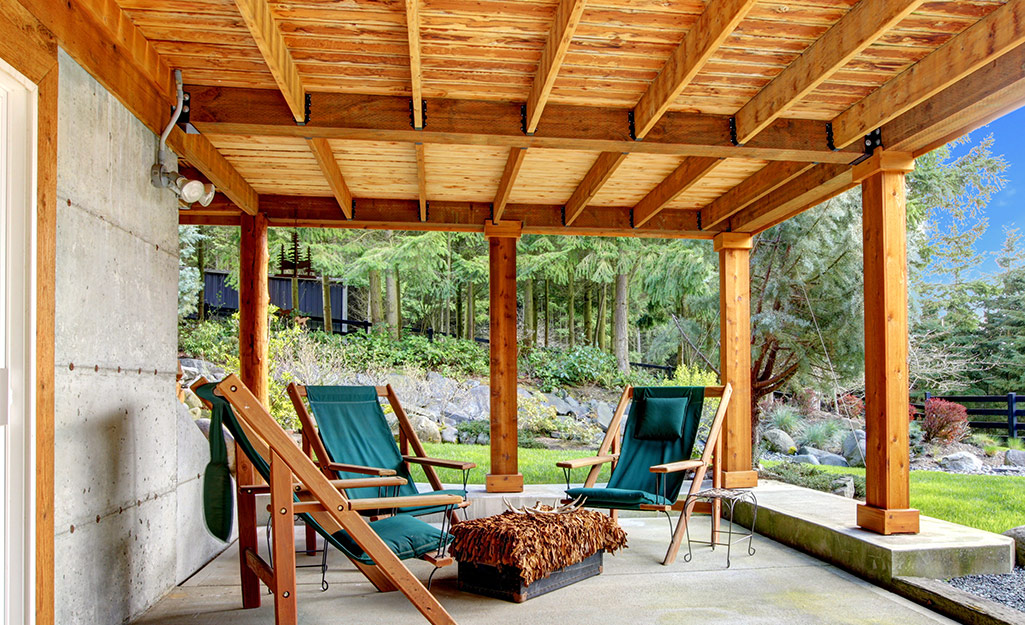 Three wood patio chairs sit on a patio underneath a deck.