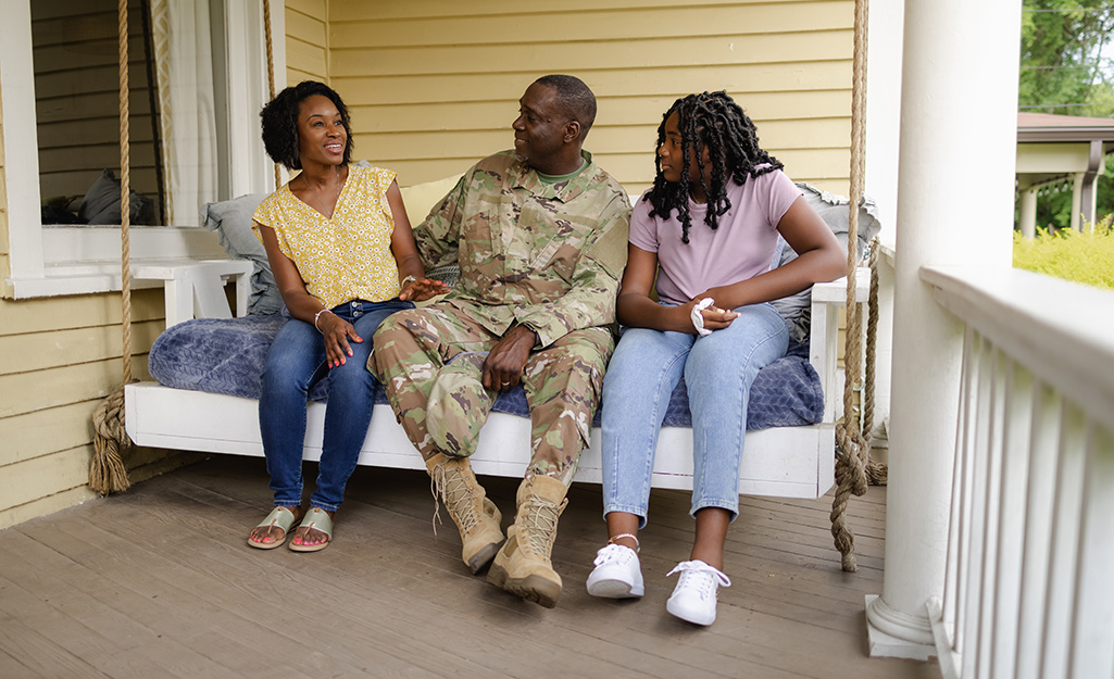 Two women and a man in a military uniform sit in a porch swing.