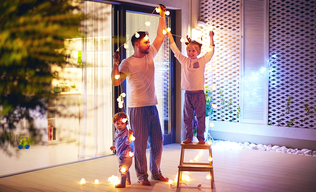 A family hanging Christmas lights outdoors.