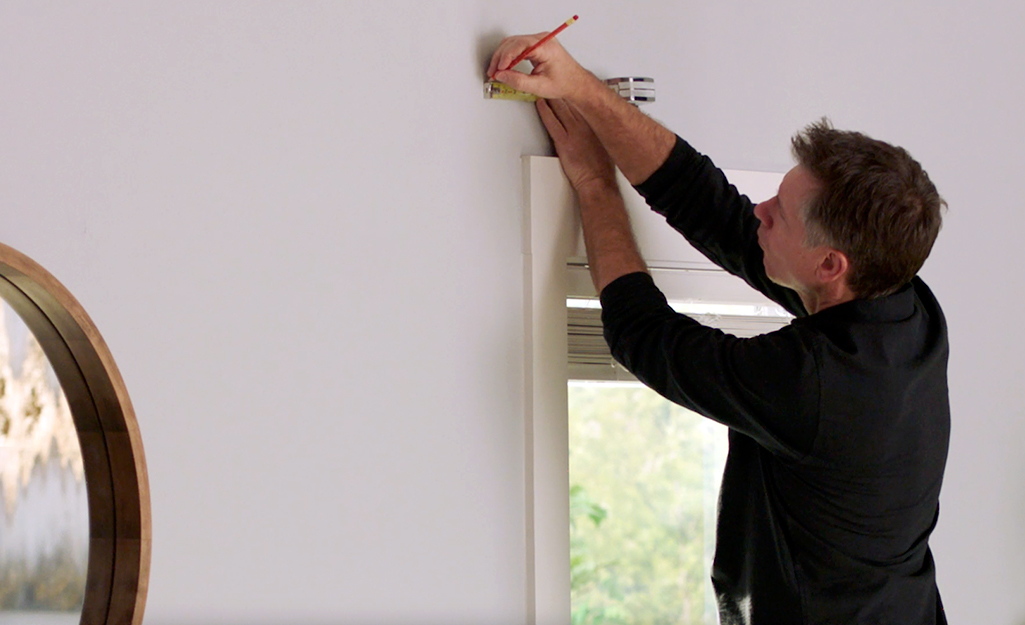 A person marking where to drill a hole on the wall for curtain rod installation