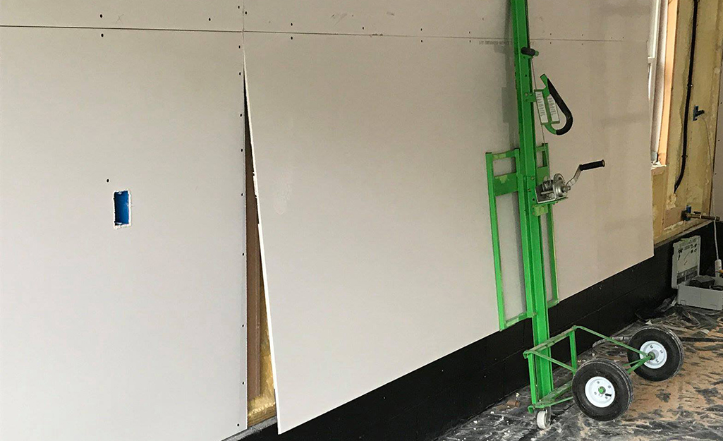 More drywall being placed on a wall using a drywall lift.