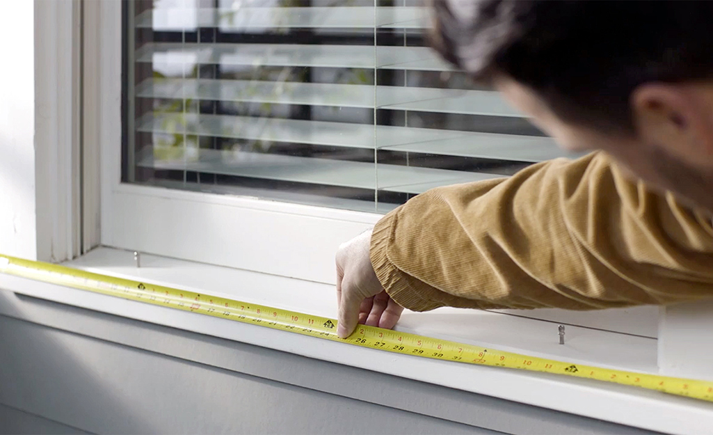 Person using a measuring tape to measure a windowsill for hanging Christmas lights