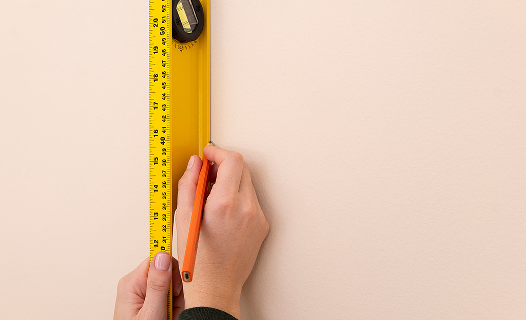 Person using measuring tape level and pencil to measure wall.