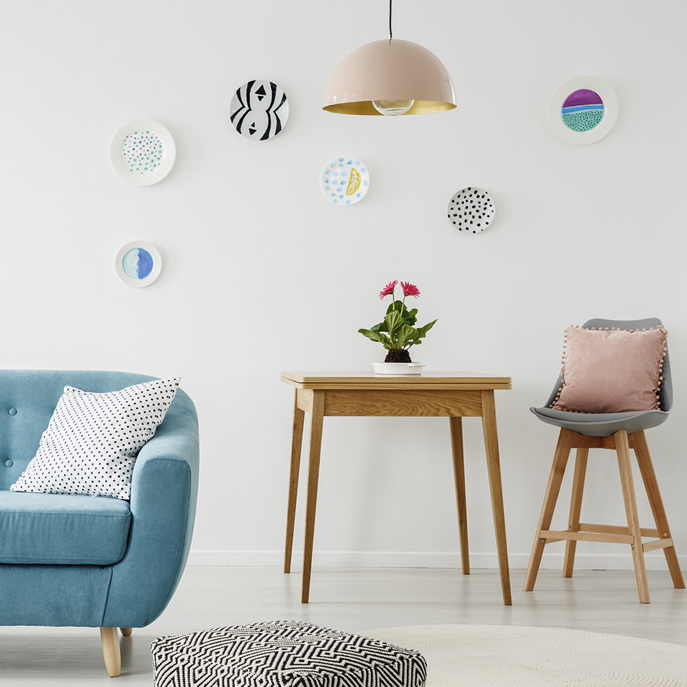 Decorative plates hung on a wall with a couch, table and chair nearby.