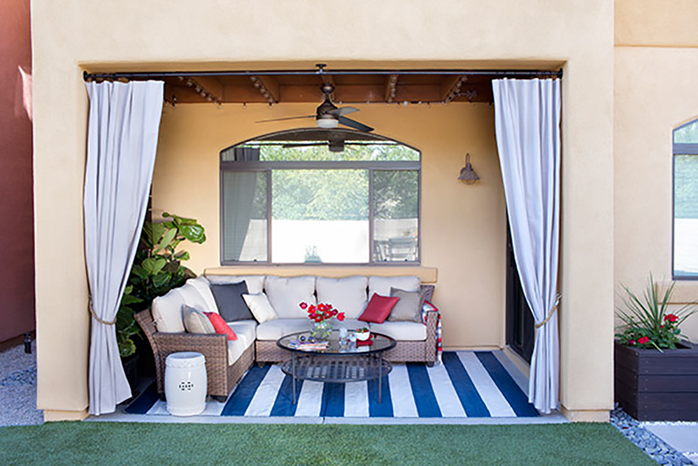 An outdoor patio decorated with a blue and white striped rug, an outdoor sectional, and string lights.