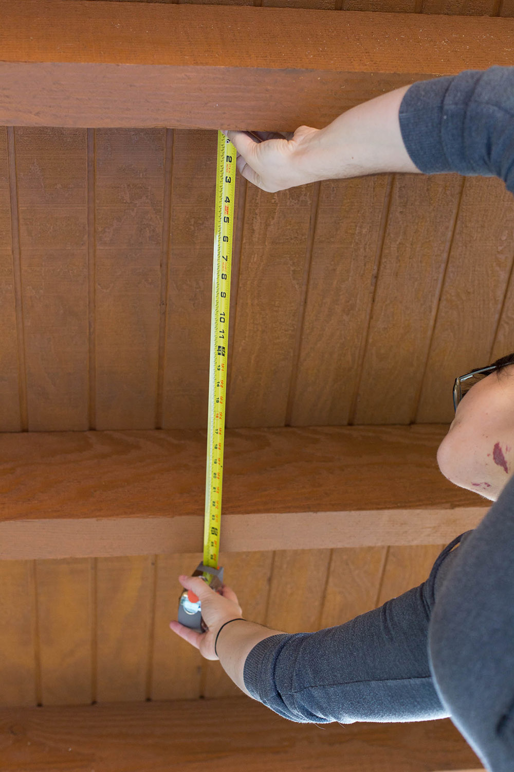 A person using a tape measurer to measure the distance between two ceiling beams.