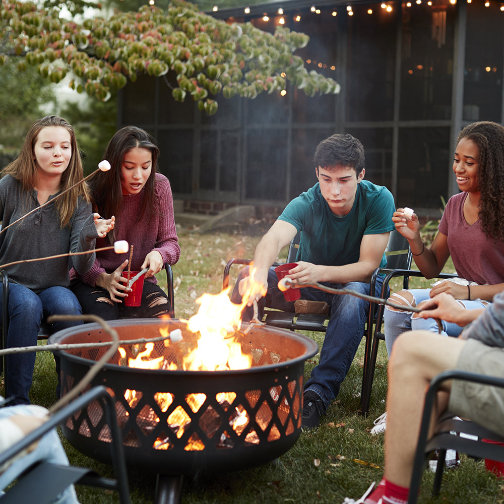 A group of people roasting marshmallows around a fire pit in a backyard.