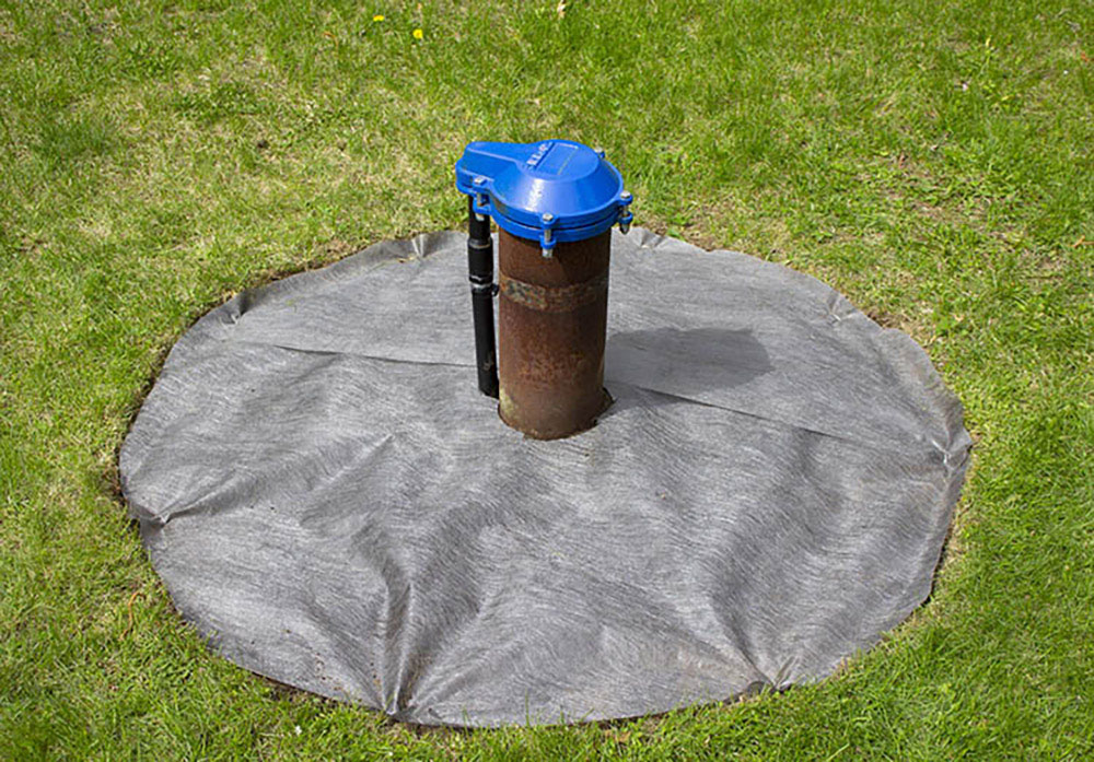 An exposed wellhead surrounded by a circle of landscape fabric.