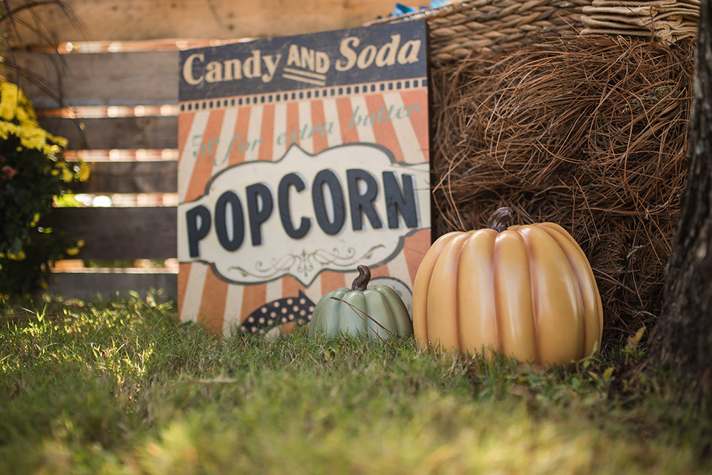 A black and orange popcorn sign next to decorative pumpkins.