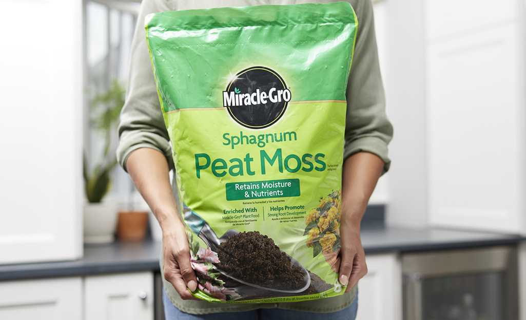 A person holding a green bag of Miracle Gro peat moss.