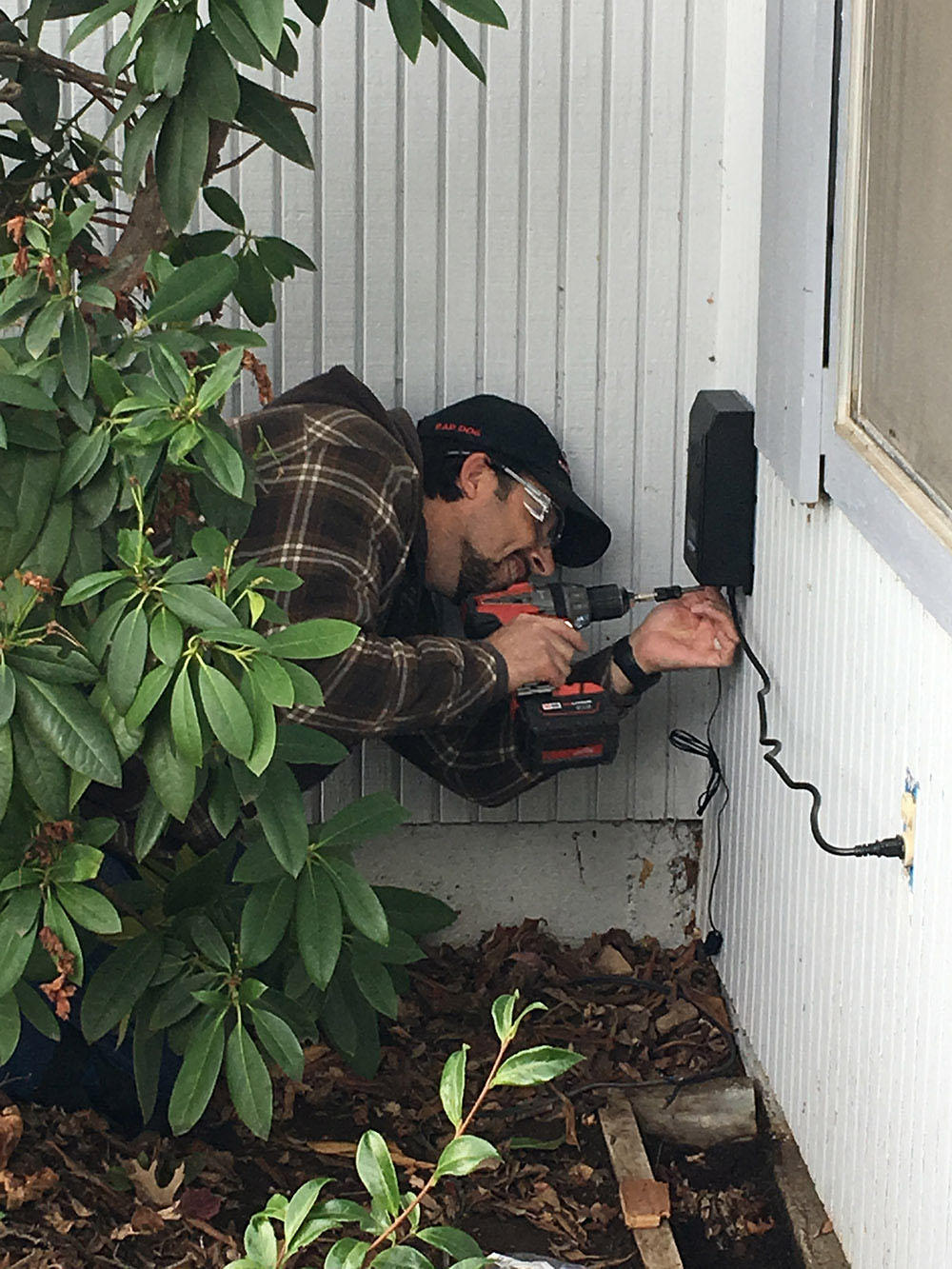 A man installing a digital transformer on the side of a house.
