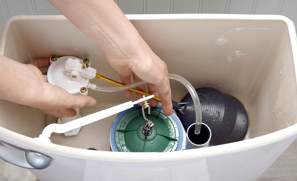 A person removes a ballcock fill valve from a toilet.