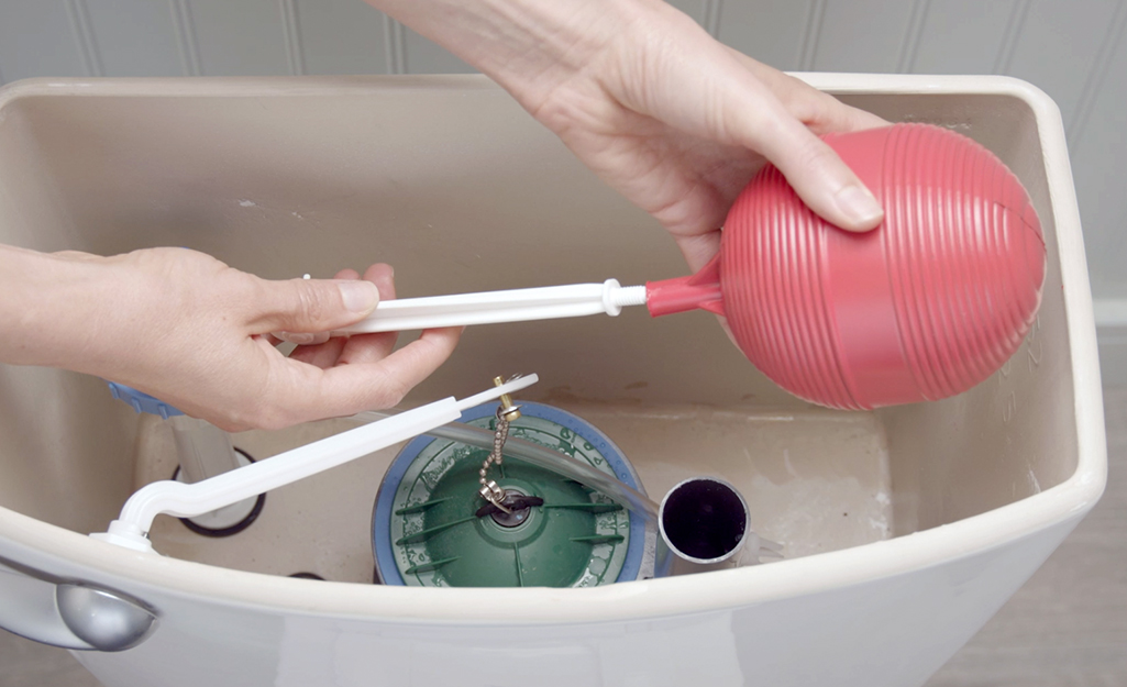 A person aligns the float arm socket for a ballcock fill valve in a toilet tank.