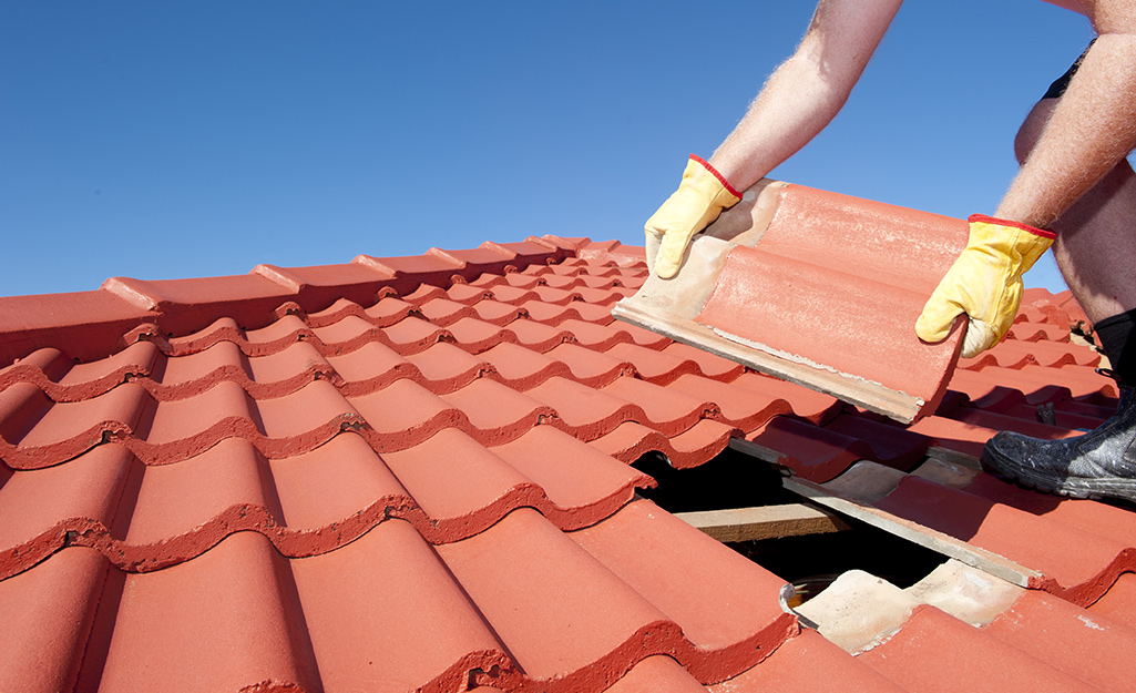 A person removes shingles from a roof.