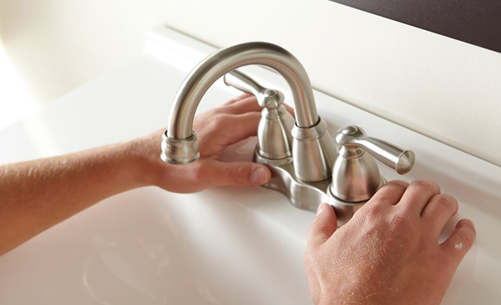 A person adjusting the position of a bathroom faucet on a sink.