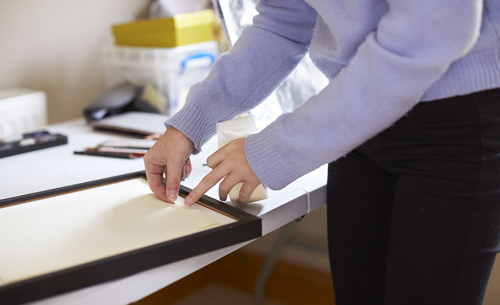 A person preparing a small frame to hold a mirror.