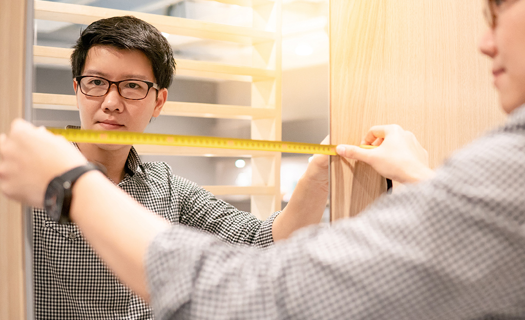 A person measuring a frameless mirror.