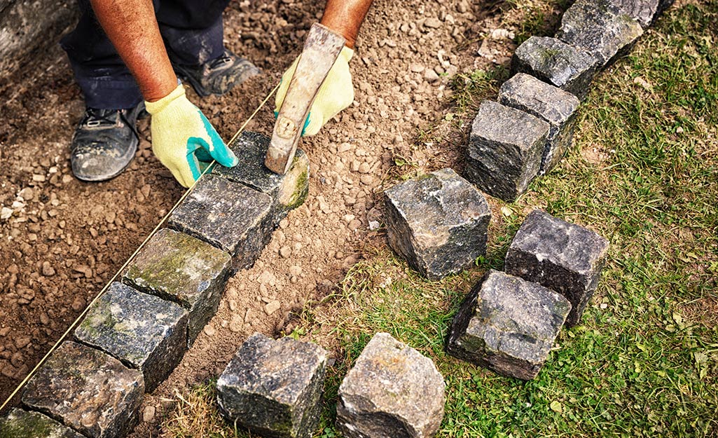 A person laying paver bricks along an edging area.