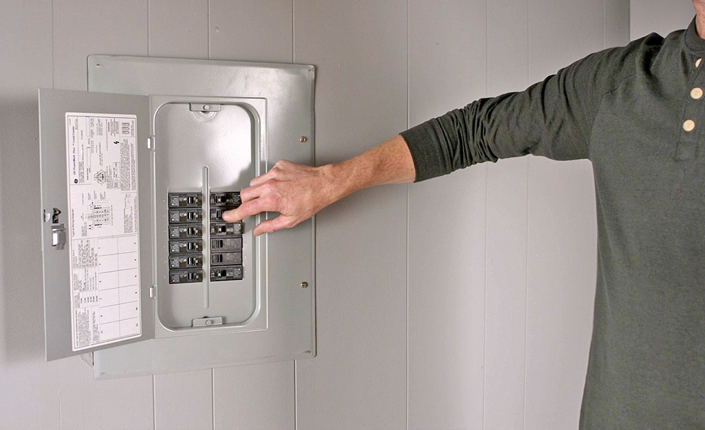 A person turning off a circuit switch in a circuit breaker. 