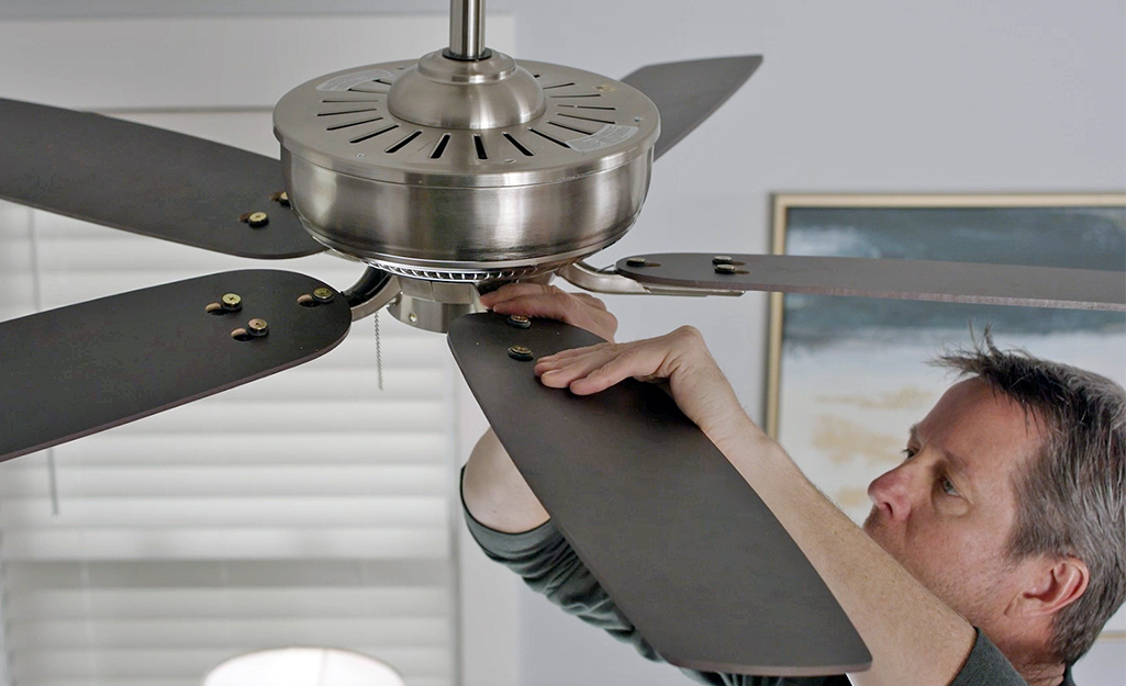 A man attaches blades to a ceiling fan. 