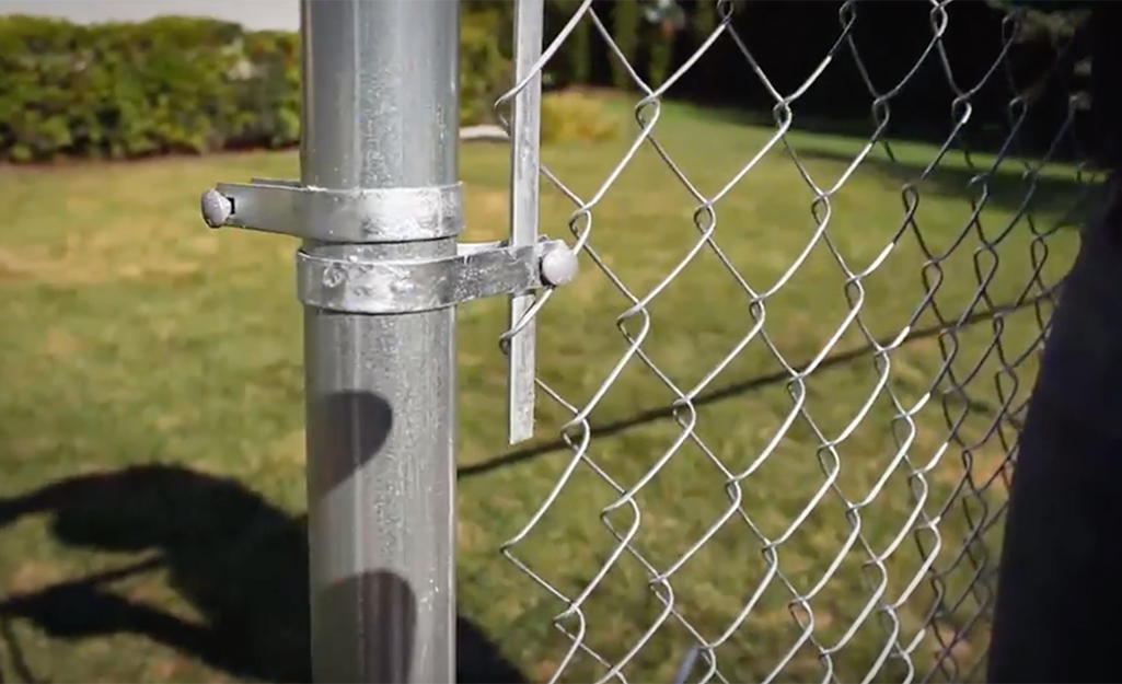 Someone attaching a tension bar to a chain link fence.