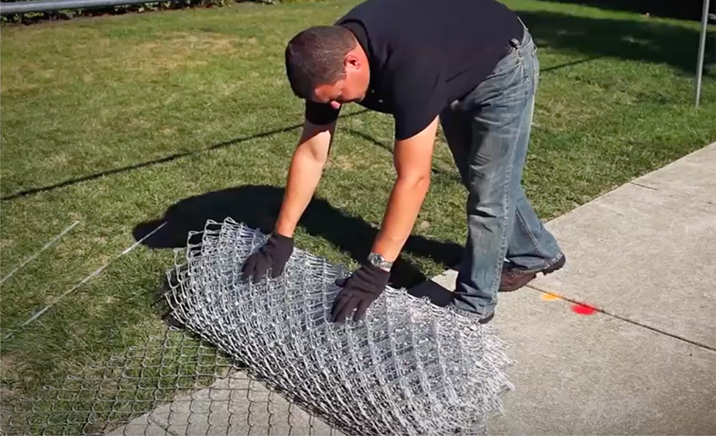 Someone unrolling chain link fence mesh.