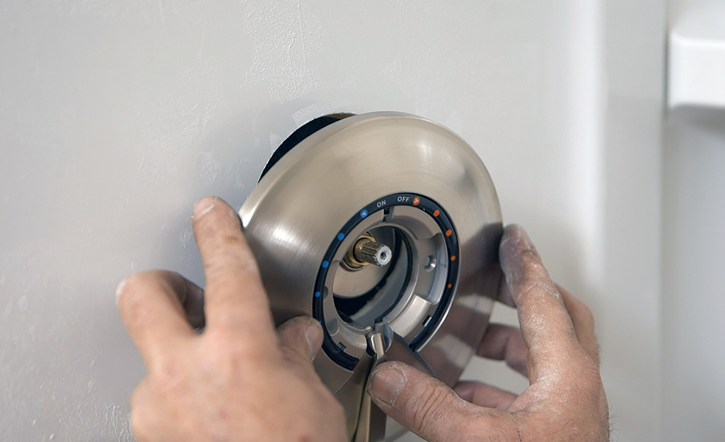A person installing the trim over the shower valve.