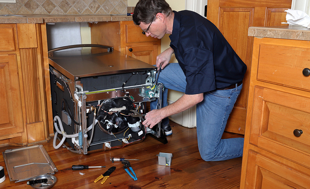 A person using a hole saw for installing dishwasher supply lines.