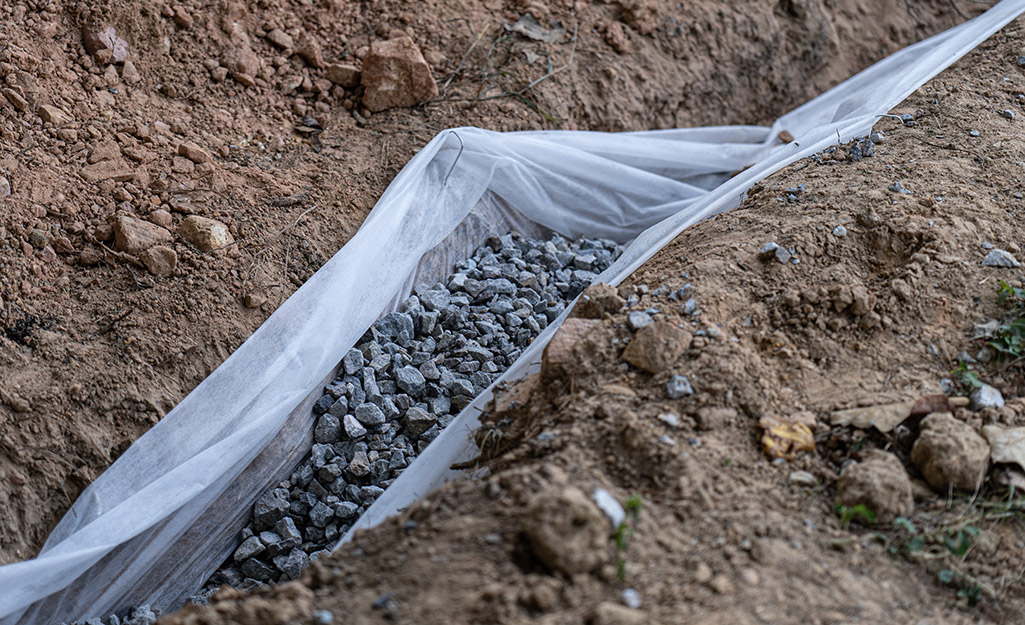 A trench lined with landscape fabric and filled with gravel.