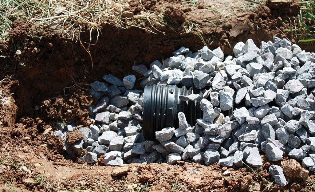 A French drain pipe opening peaking out of a mound of gravel.