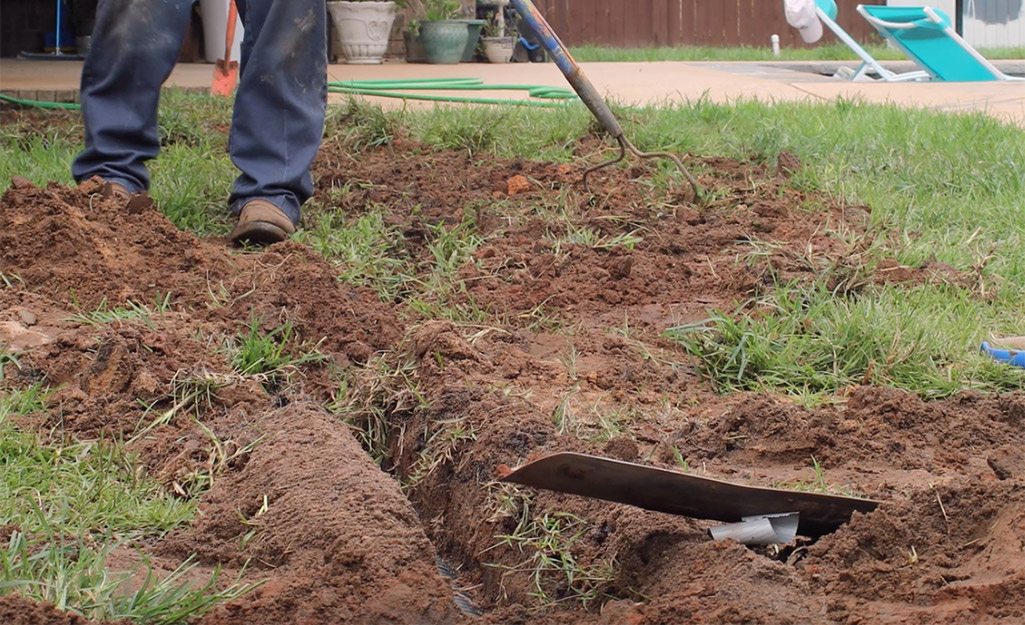 A person filling a trench with topsoil.