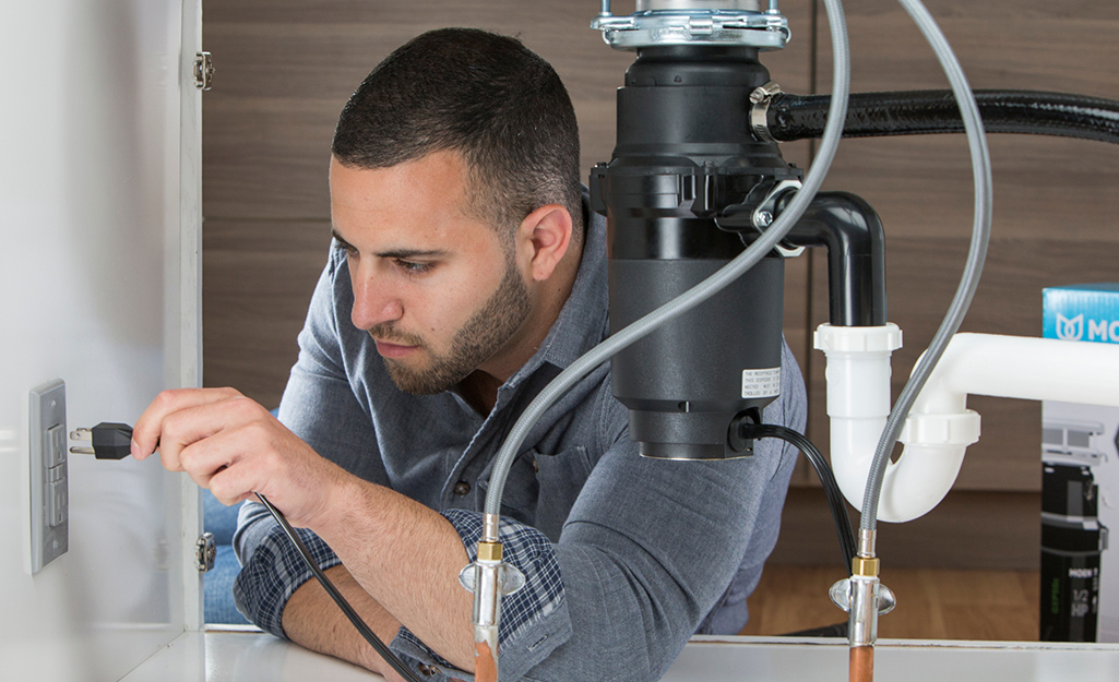 A person plugs in a garbage disposal.