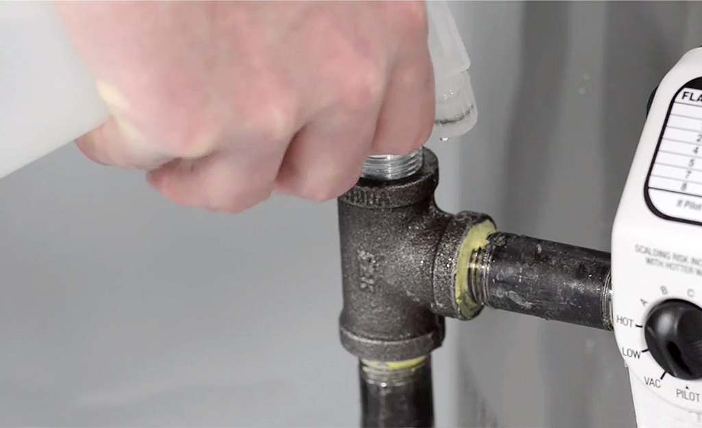 A person uses a solution of soap and water test a water heater gas line for leaks.
