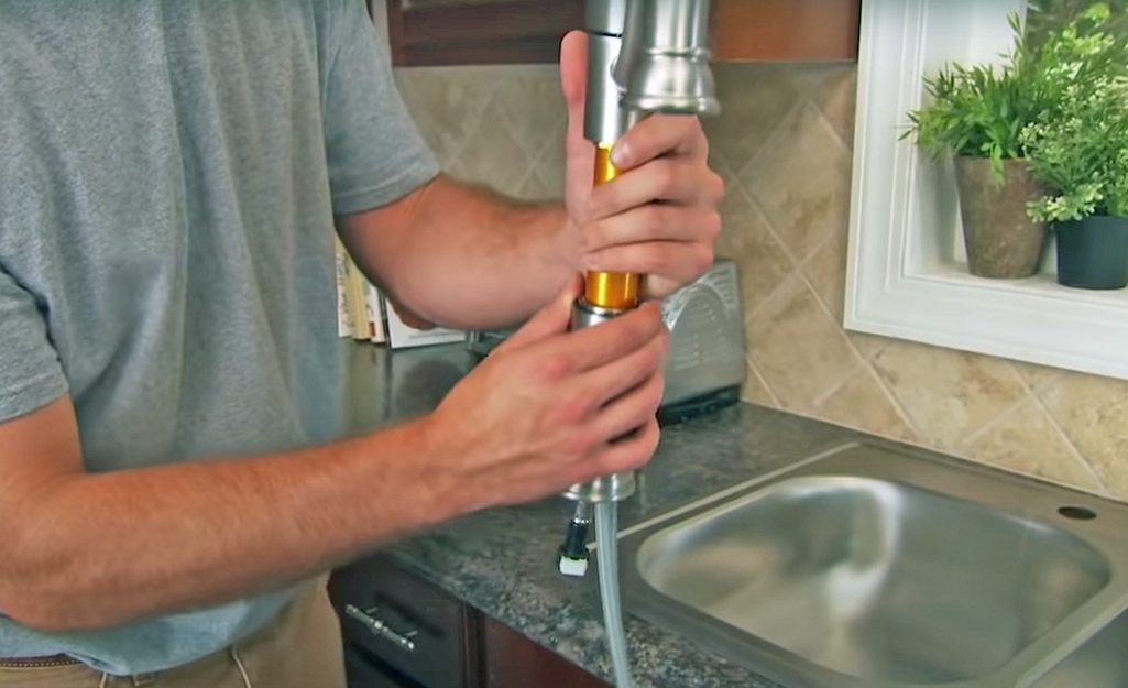 A person installs a new kitchen faucet. 