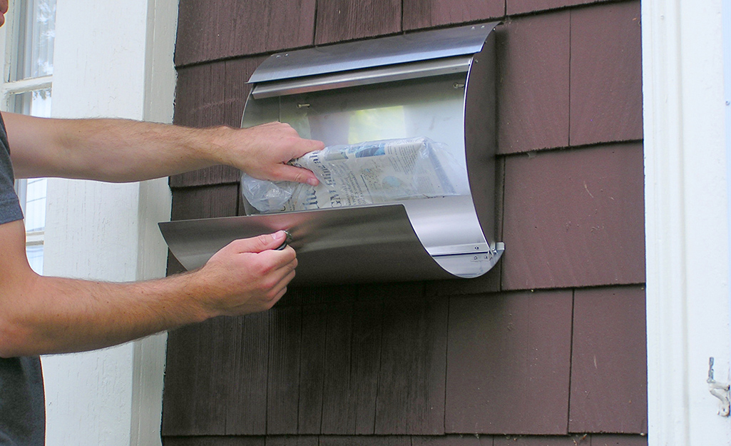 A person getting mail from a wall mounted mailbox.