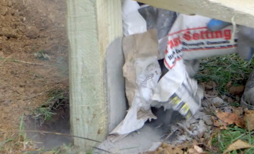 A person pouring concrete into a post hole.