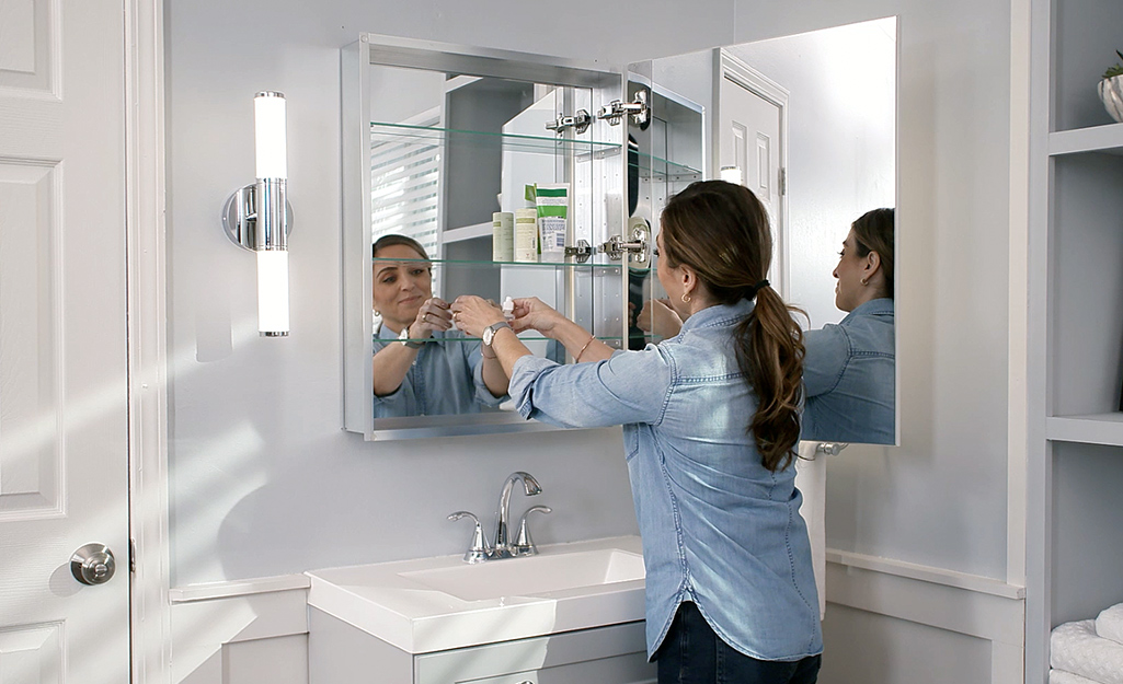 A woman places items in the open surface-mount medicine cabinet.