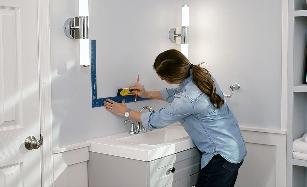 A woman measuring a wall for the recessed medicine cabinet installation.