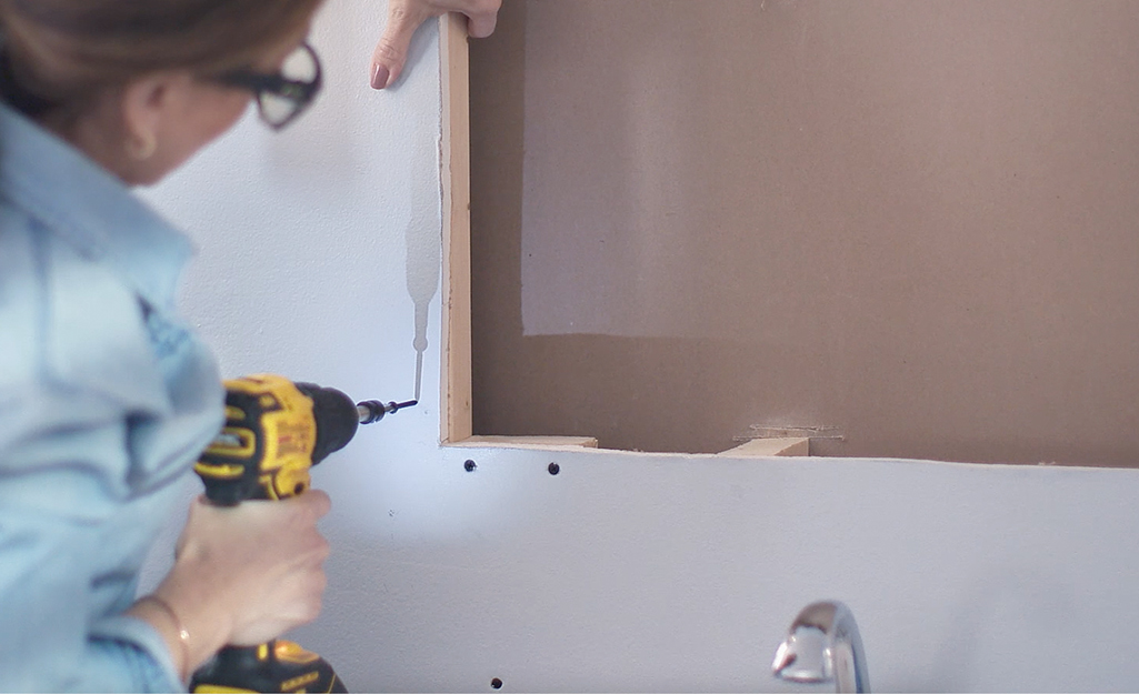 Someone uses a drill to drive screws into drywall.