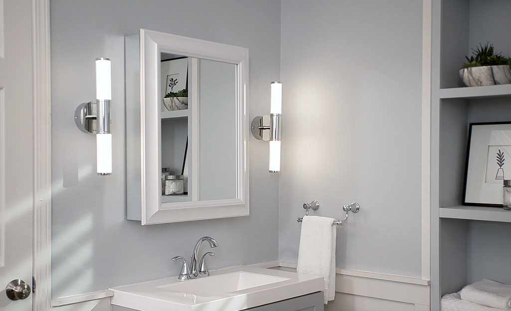 A medicine cabinet hangs between two light sconces on a gray wall.