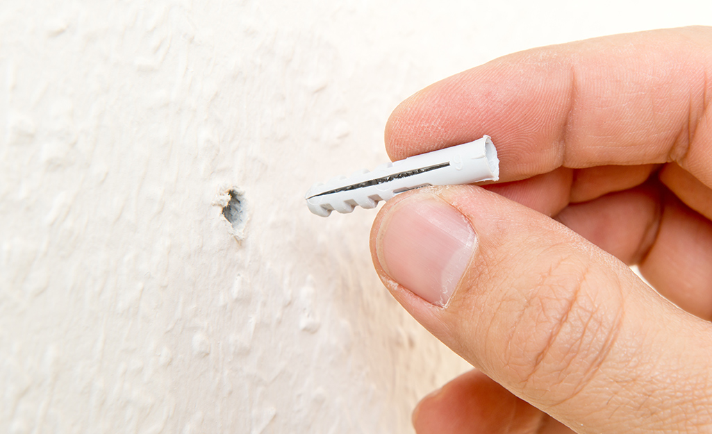 Someone inserting anchor screws into predrilled holes in a wall. Someone inserting anchor screws into predrilled holes in a wall.