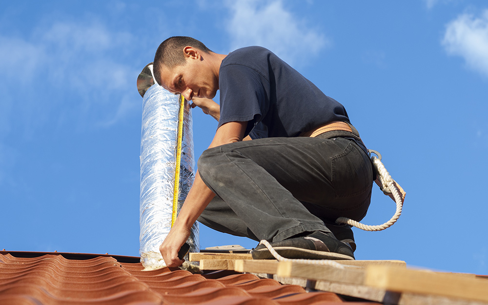 A man installing a vent on a metal roof. A man installing a vent on a metal roof.