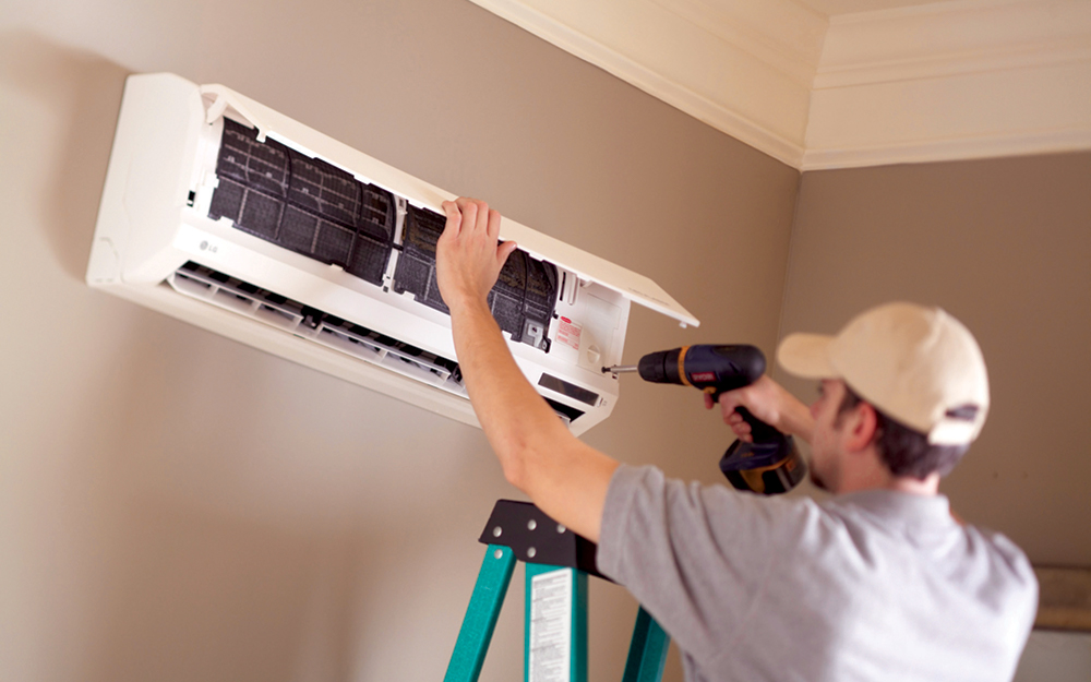 A man drilling parts of a mini split air conditioner together inside the home